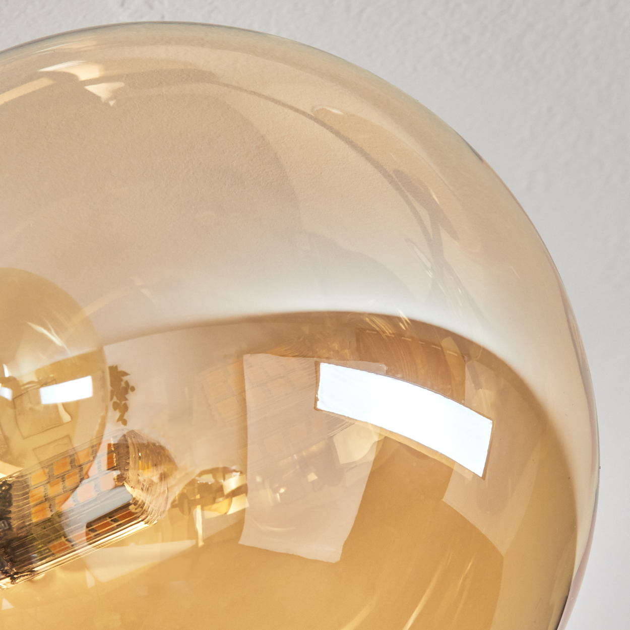 Nahaufnahme einer transparenten, bernsteinfarbenen Glaskugel. Reflexionen der Umgebung sind im Glas sichtbar. Der Hintergrund ist hell.