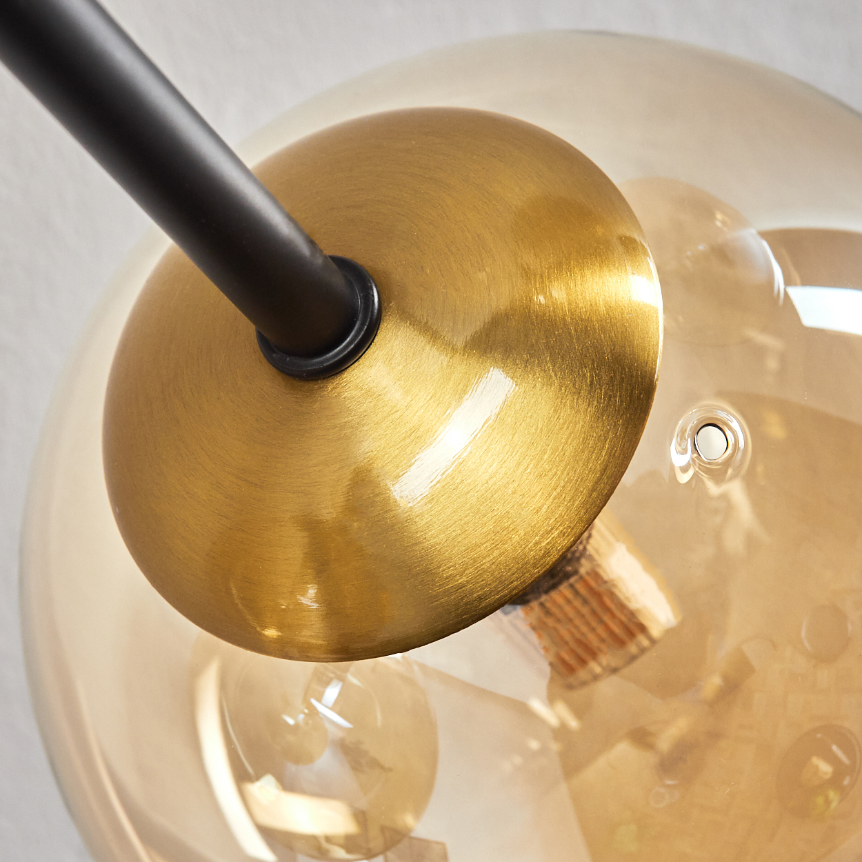Nahaufnahme einer modernen Lampe. Ein schwarzer Arm trägt eine goldene Scheibe und eine transparente, bernsteinfarbene Glaskugel. Innenbeleuchtung.