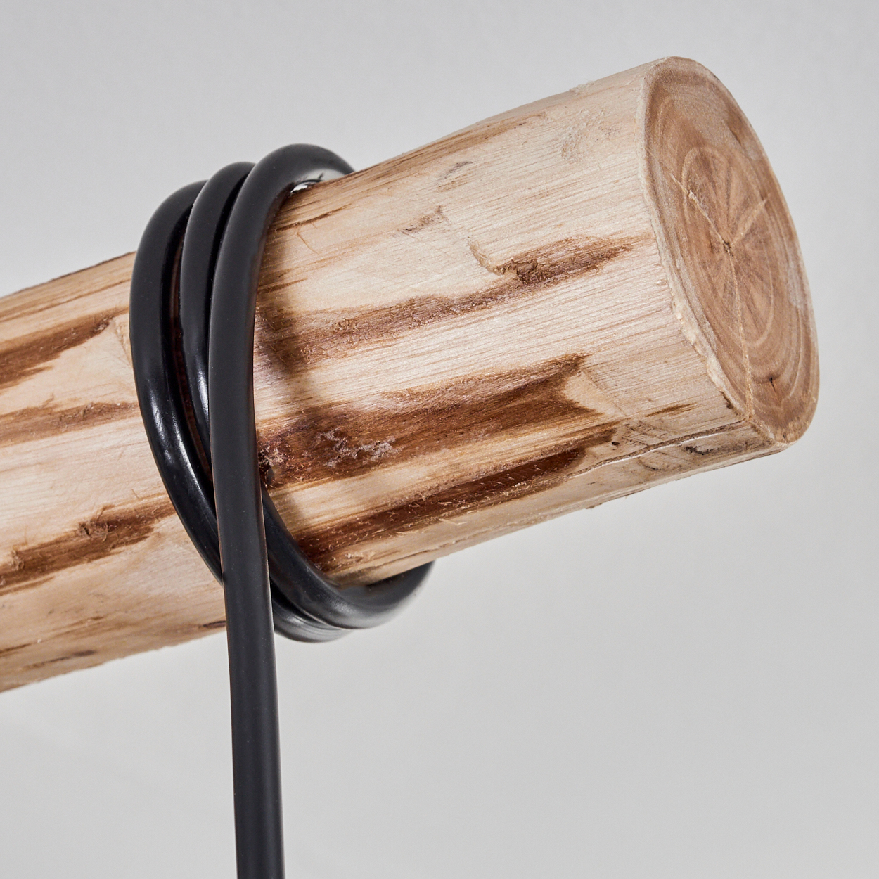Ein Holzstamm mit einem schwarzen Kabel darum gewickelt. Der Stamm ist hellbraun und hat eine raue Textur. Das Kabel ist glänzend und glatt.