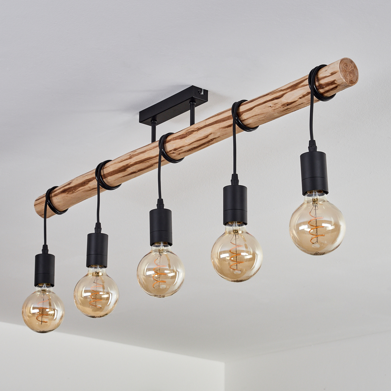 Eine Deckenleuchte aus Holzbalken mit fünf Edison-Glühbirnen. Der Balken ist hellbraun, die Birnen sind rund und orange, hängen an schwarzen Kabeln.