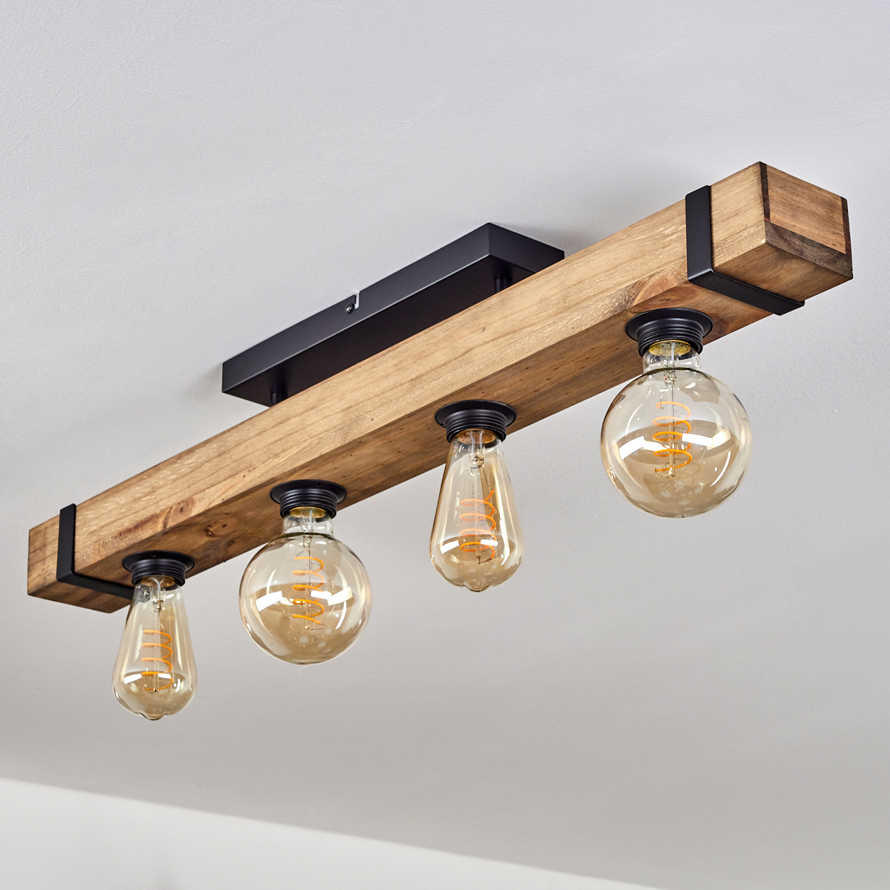 Ein Holzbalken mit vier Glühbirnen, die von der Decke hängen. Die Birnen sind rund und tropfenförmig, mit sichtbaren Glühfäden.