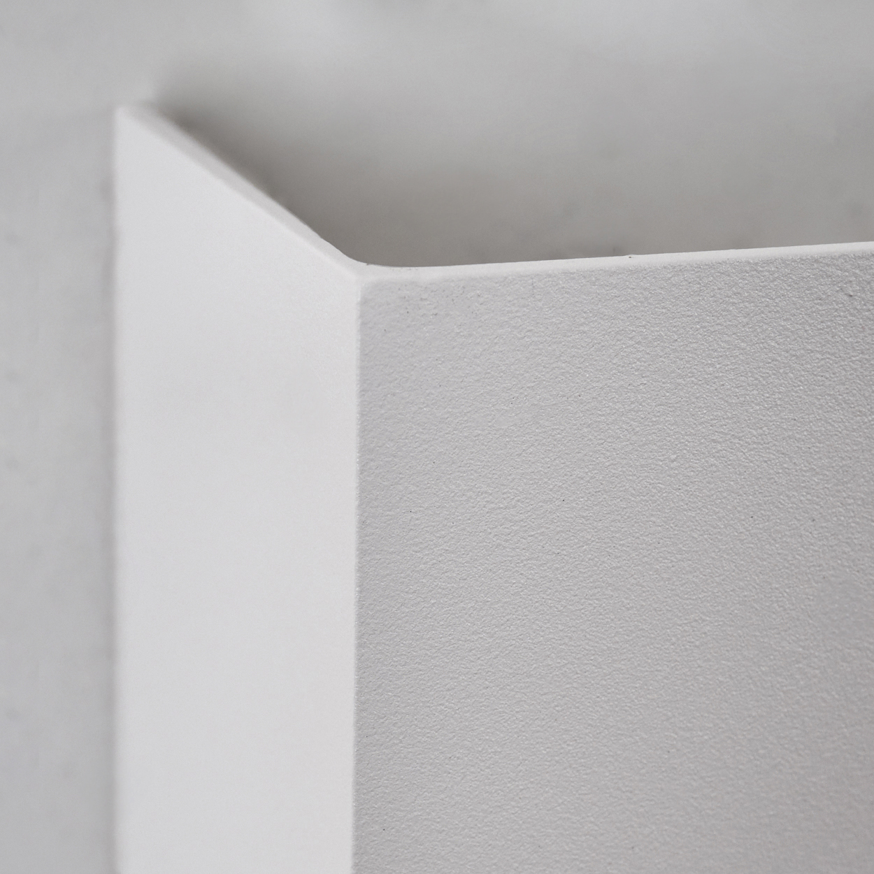 Nahaufnahme einer weißen, eckigen Wand. Die Wand hat eine strukturierte Oberfläche. Der Hintergrund ist ein weicheres Weiß, das eine Ecke andeutet.