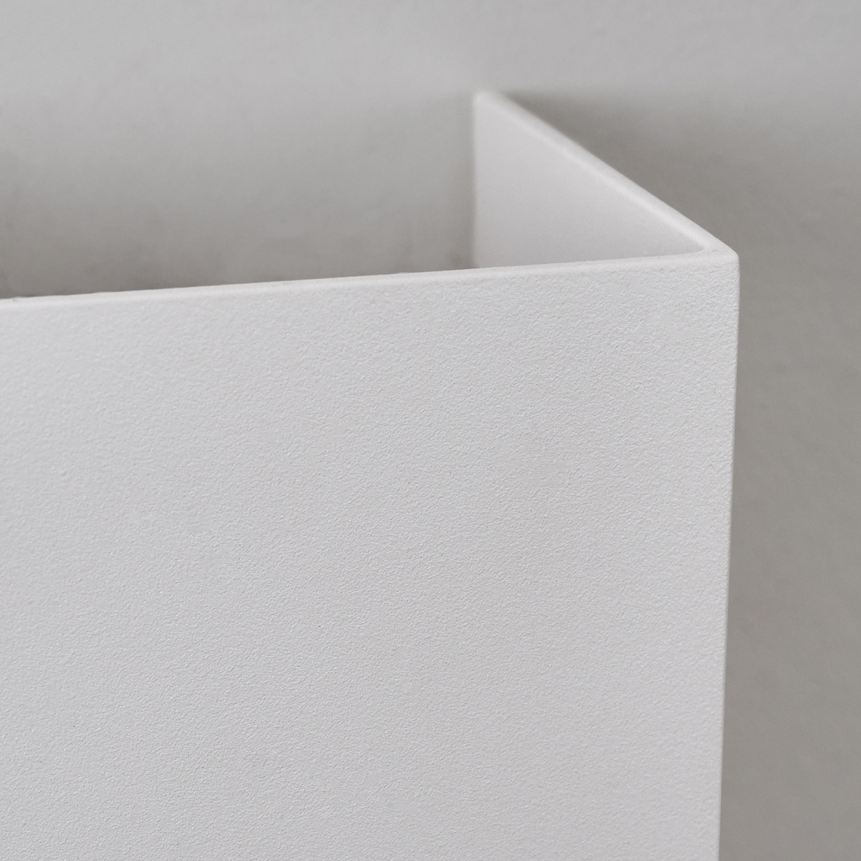 Nahaufnahme einer weißen, strukturierten Ecke, möglicherweise einer Box oder Wand. Der Hintergrund ist ein schlichtes, helleres Weiß.