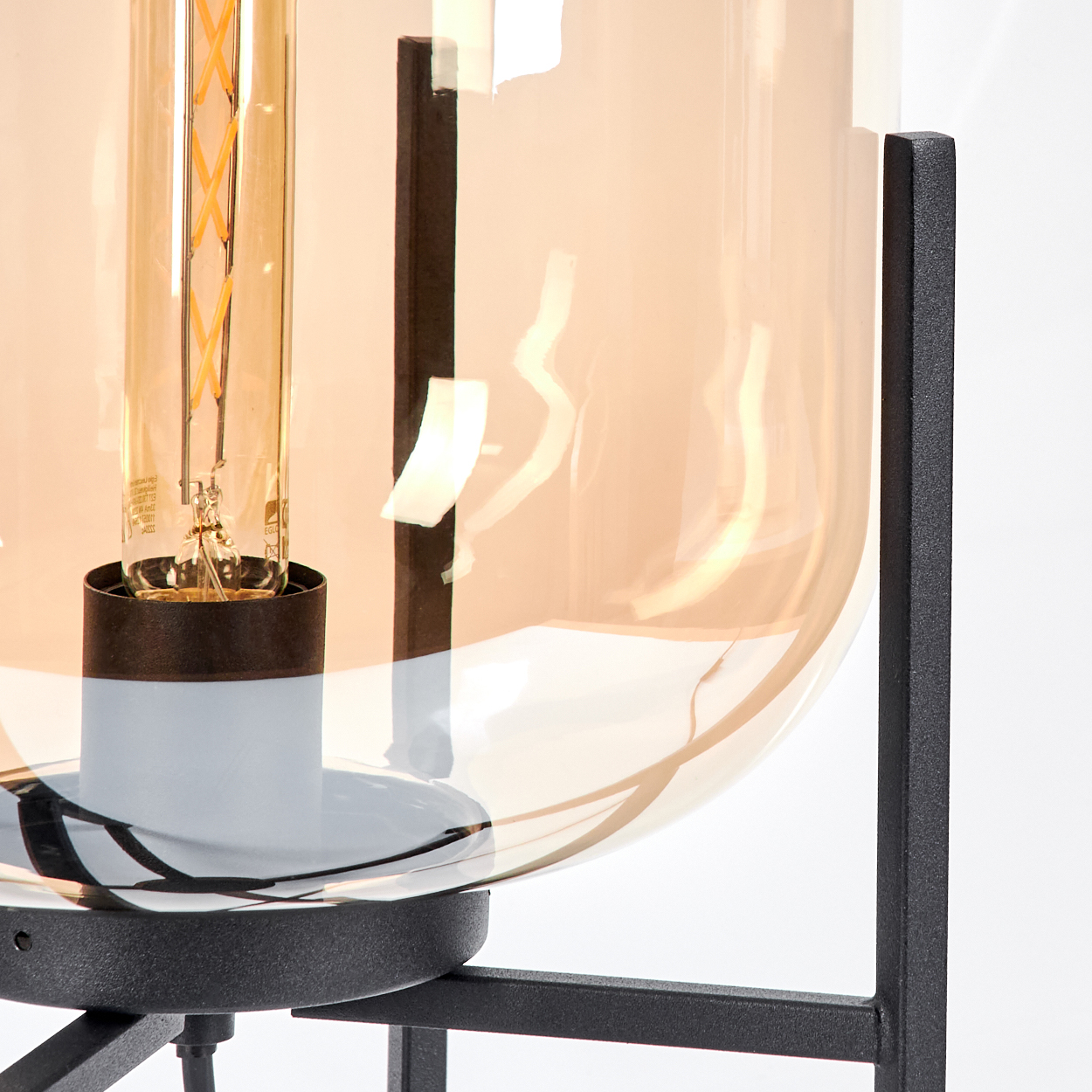 Nahaufnahme einer modernen Lampe mit großem bernsteinfarbenem Glasschirm. Eine Glühbirne ist sichtbar. Schwarzer Metallrahmen.