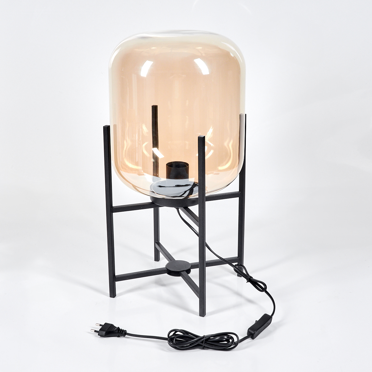Eine moderne Lampe mit einem pfirsichfarbenen Glasschirm steht auf einem schwarzen Metallrahmen. Ein schwarzes Netzkabel führt zu einem Stecker.