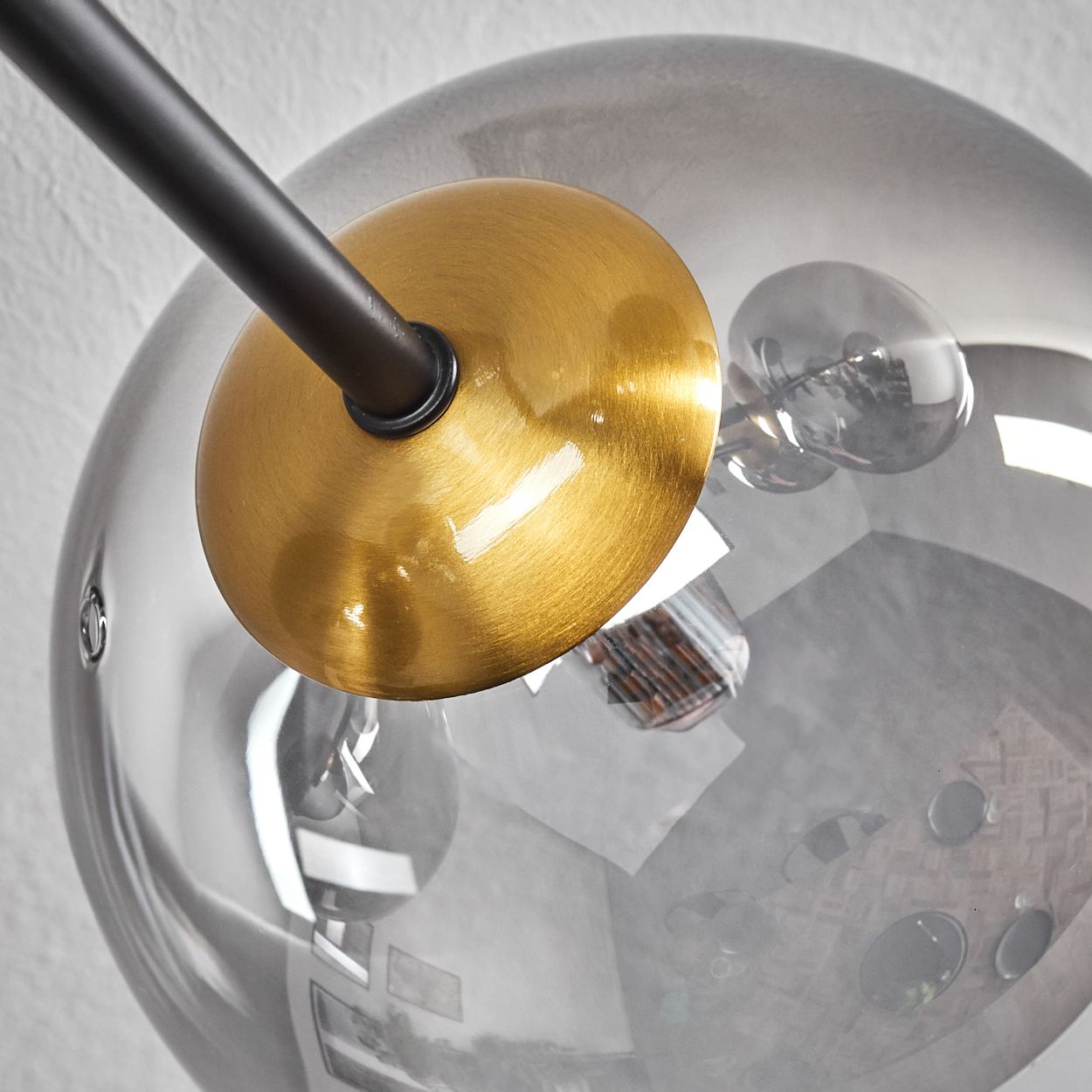 Nahaufnahme einer modernen Lampe. Sie hat eine goldfarbene Scheibe, einen schwarzen Arm und eine transparente Glaskugel.