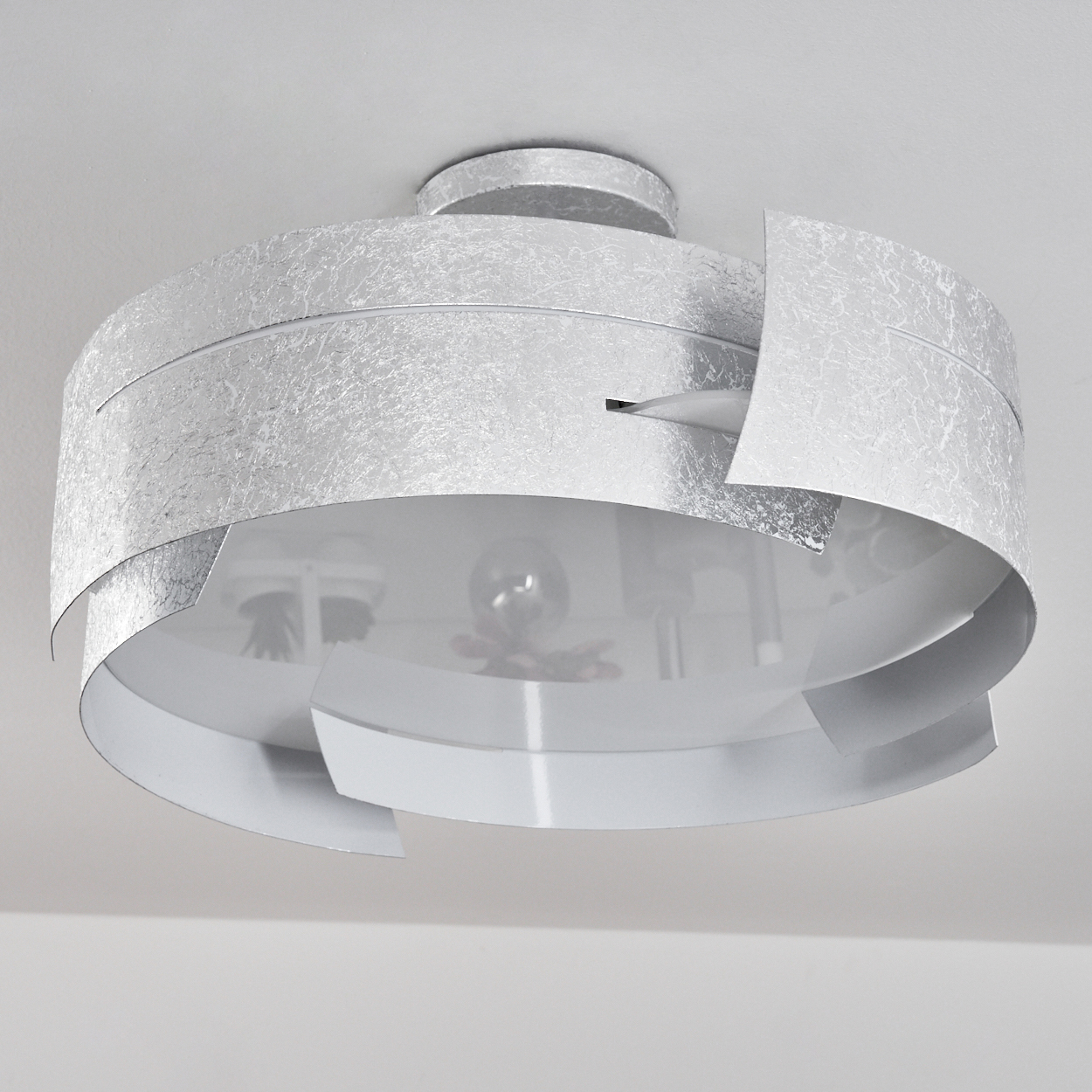 Eine silberne Deckenleuchte. Sie hat ein kreisförmiges Design mit geschichteten Abschnitten und einer strukturierten Oberfläche. Das Licht ist an einer weißen Decke befestigt.