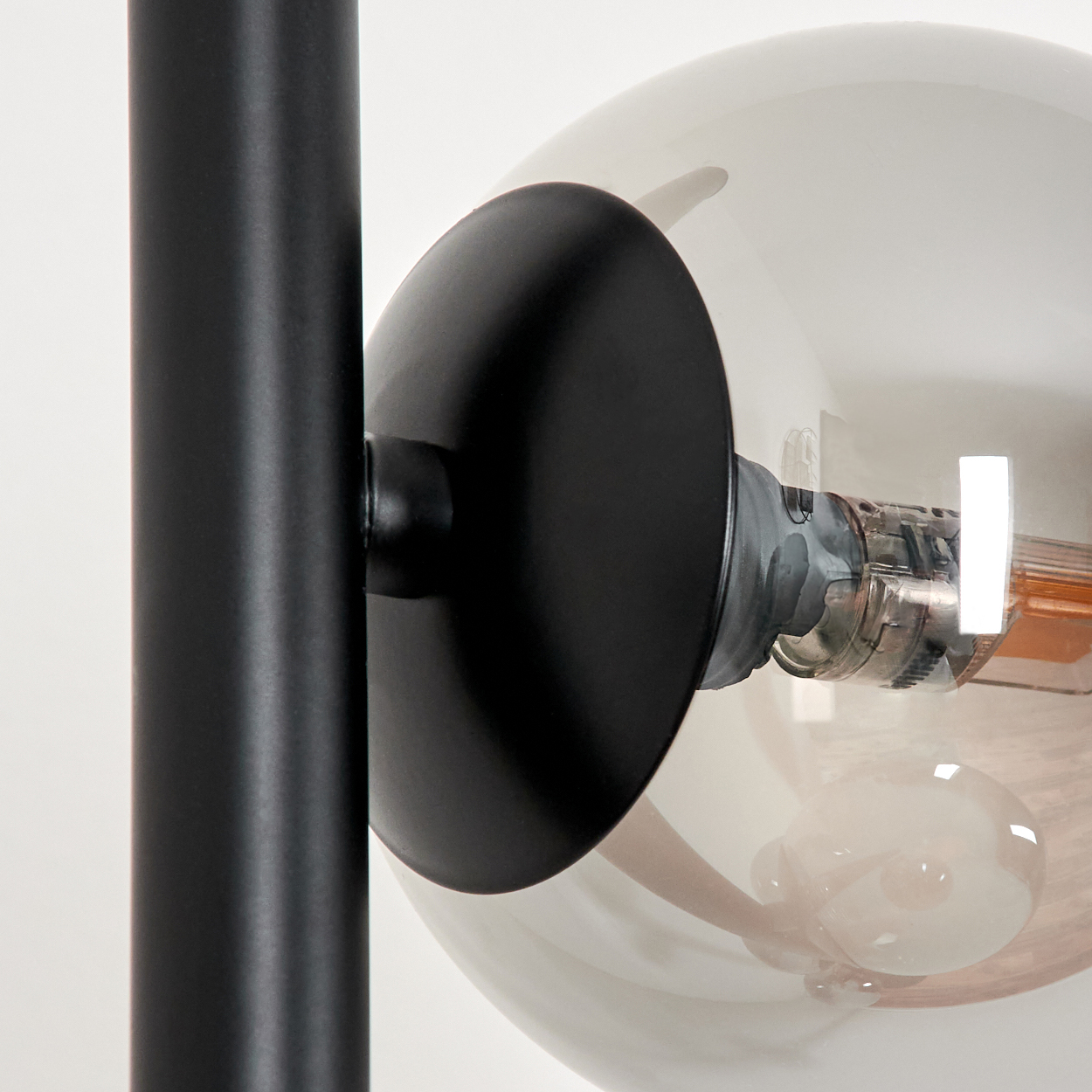 Nahaufnahme einer modernen Lampe. Ein schwarzer Metallträger hält eine große, klare Glaskugel mit einer Glühbirne.