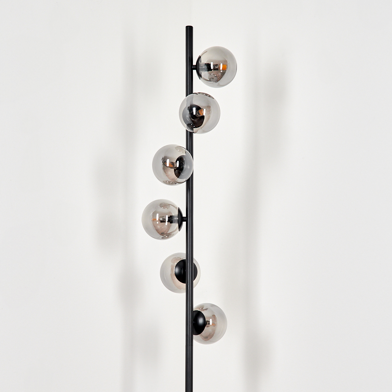Eine moderne Stehlampe mit sechs kugelförmigen, verspiegelten Glasschirmen an einer schwarzen Metallstange vor weißer Wand.