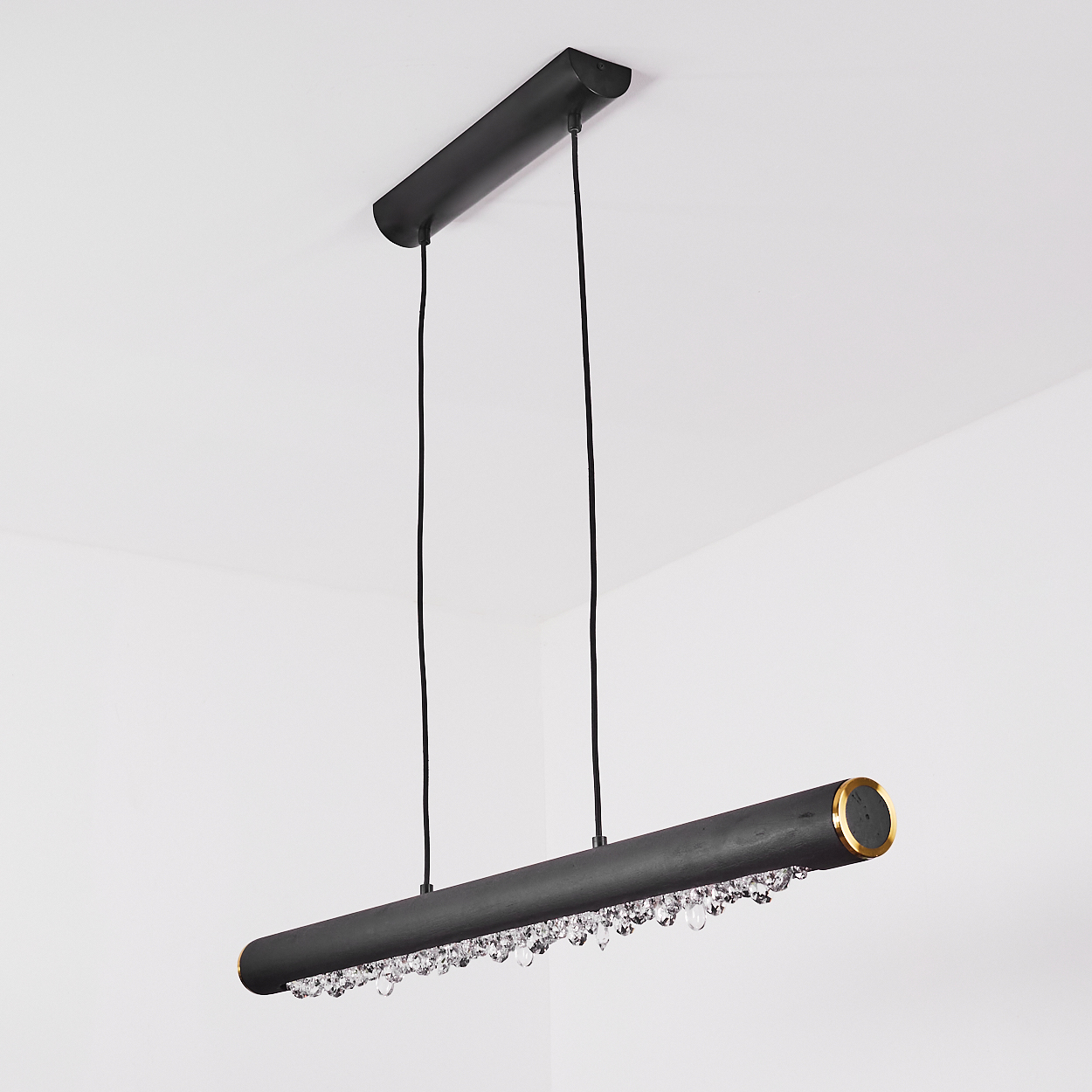Eine moderne, schwarze zylindrische Hängelampe hängt von der Decke. Sie hat goldene Akzente und Kristallanhänger, vor weißem Hintergrund.