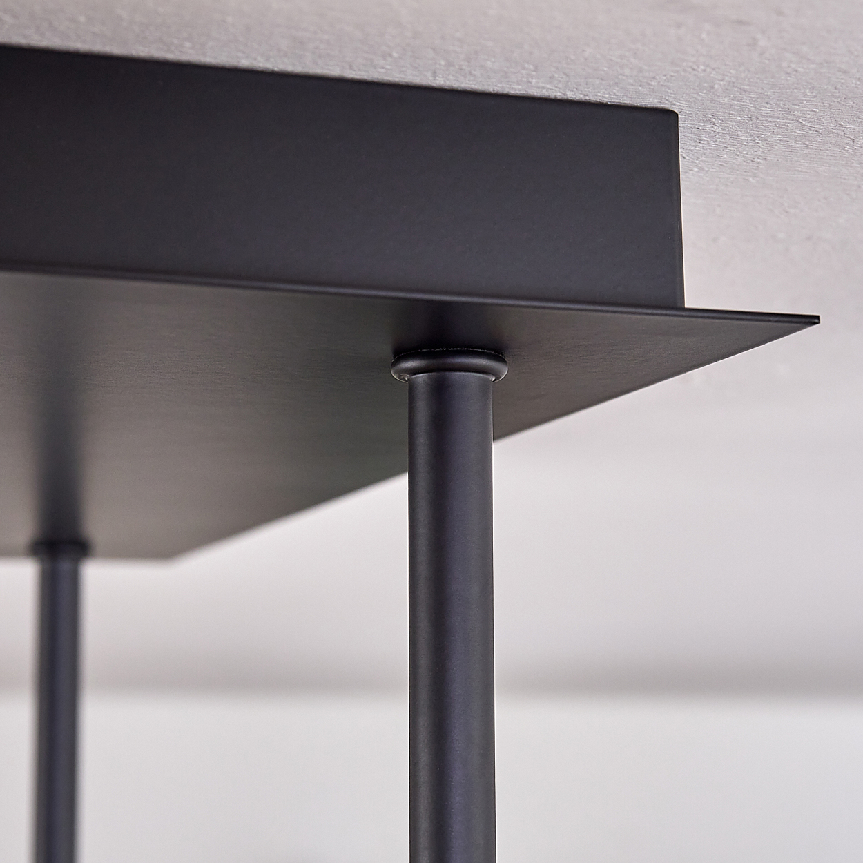 Nahaufnahme eines modernen, schwarzen Metallregals, das von zylindrischen Beinen getragen wird. Das Regal ist quadratisch mit minimalistischem Design an einer weißen Wand.