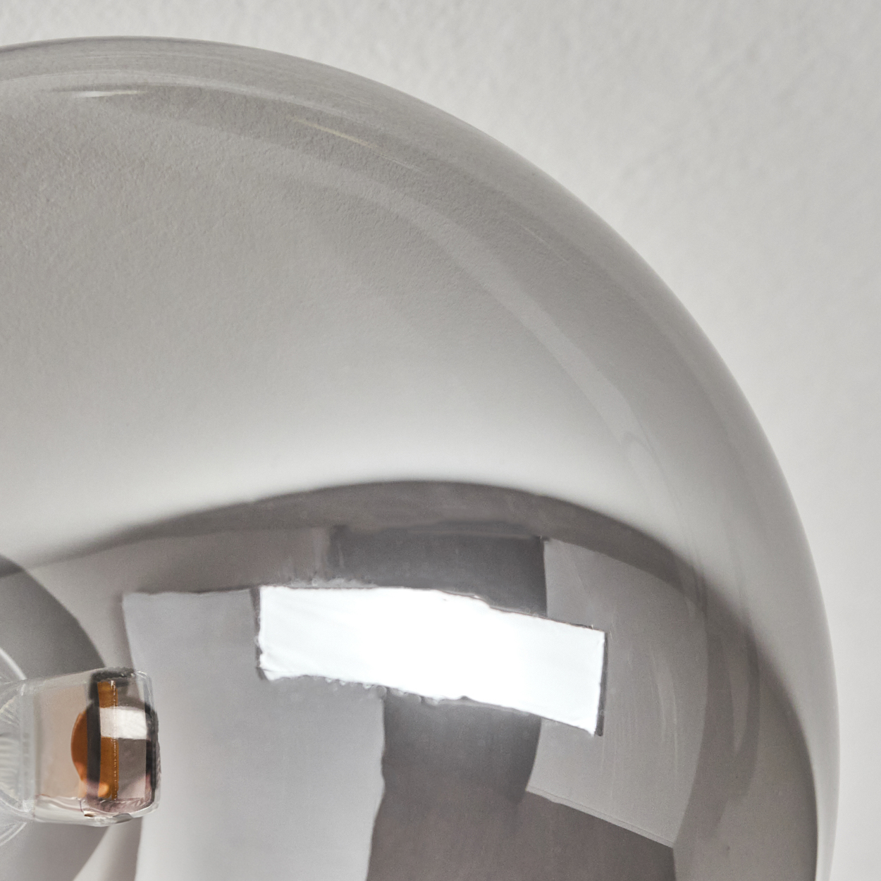 Nahaufnahme einer gekrümmten, grauen, reflektierenden Oberfläche. Sie hat eine rechteckige Öffnung. Ein kleines, transparentes Objekt befindet sich links.