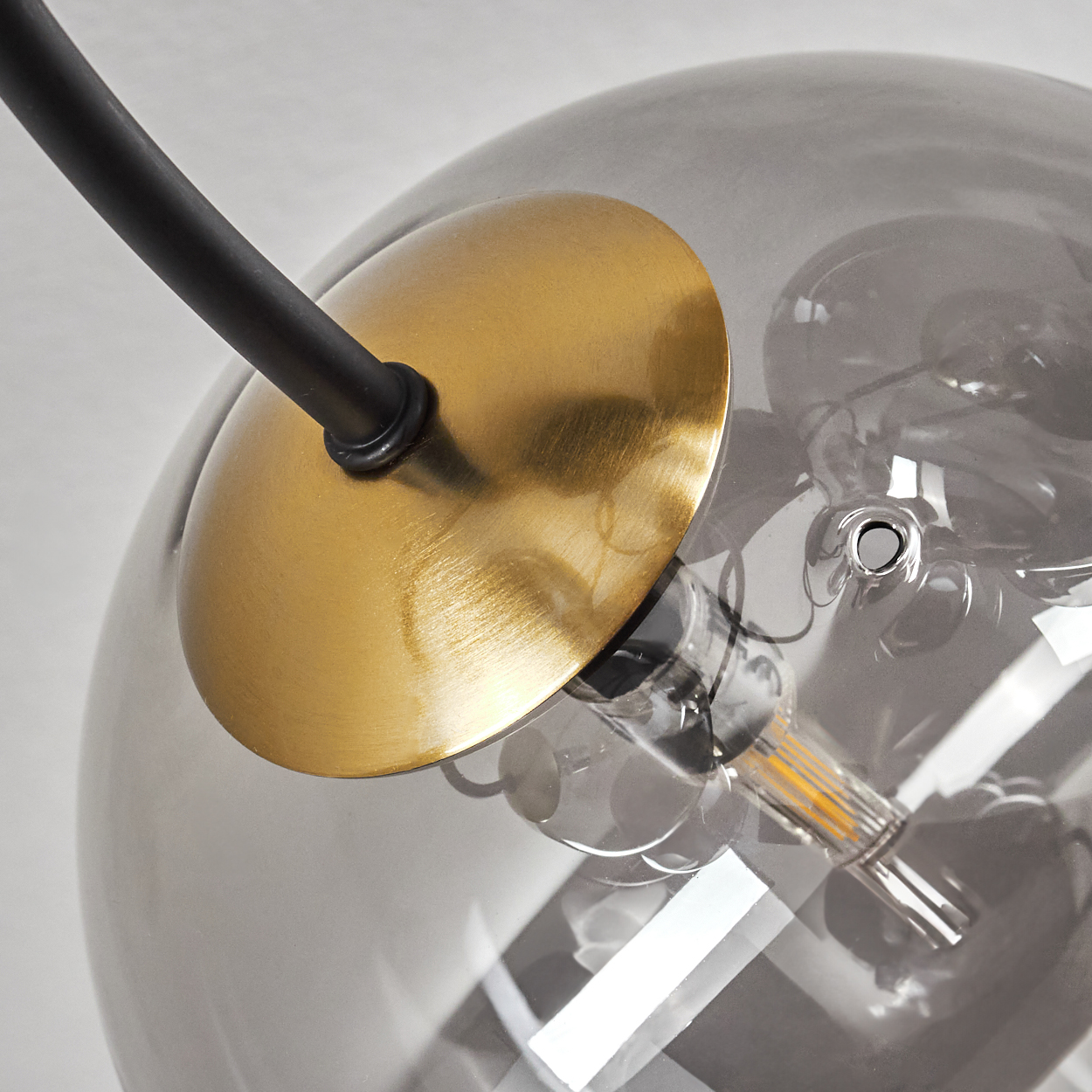 Nahaufnahme einer modernen Lampe. Ein rauchfarbener Glaskolben mit einer goldfarbenen Metallscheibe und einem schwarzen Arm. Sichtbare Glühbirne.