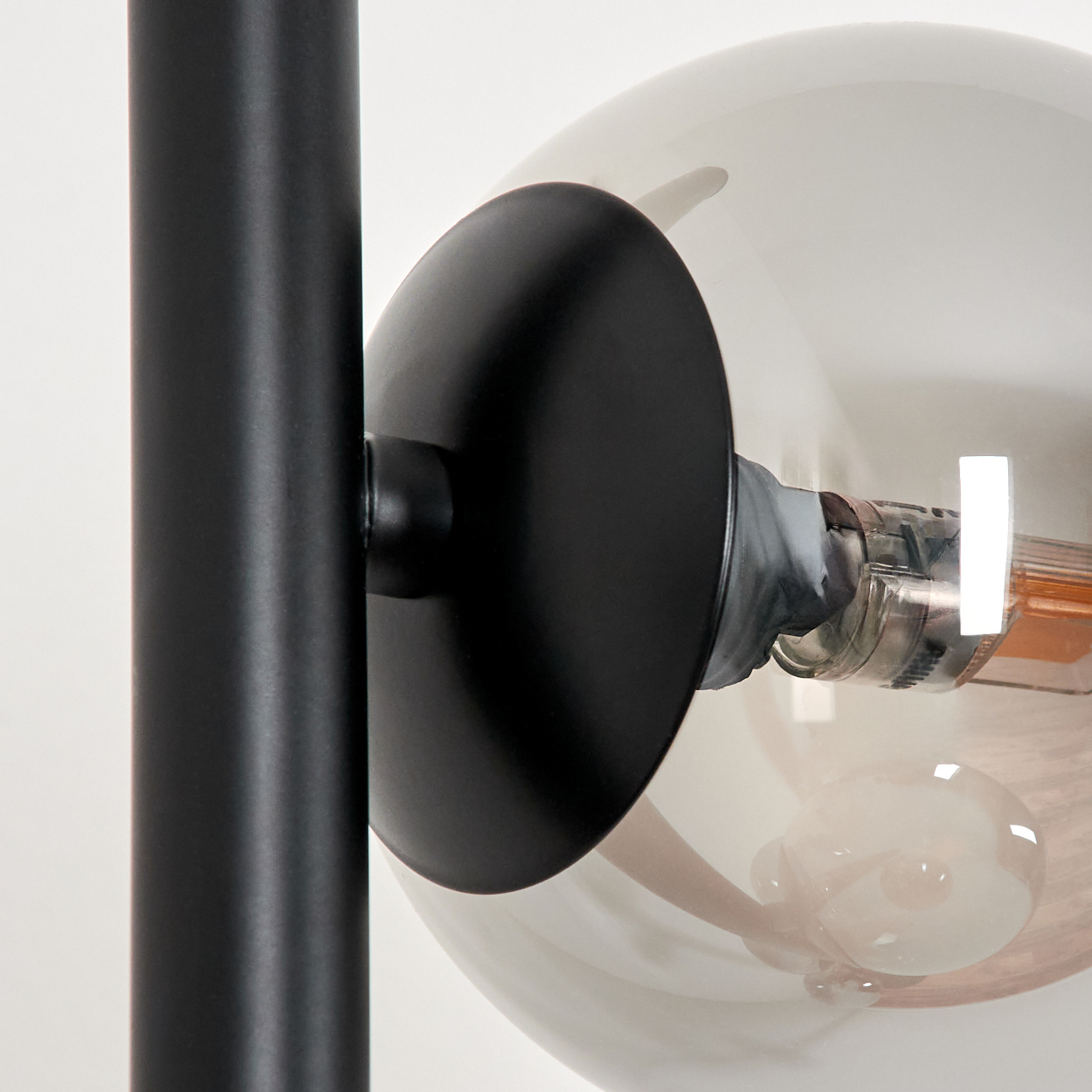 Nahaufnahme einer Lampe. Schwarzer Metallpfosten und -schirm mit klarer Glühbirne. Die Glühbirne ist rund und hat einen glühenden Faden.