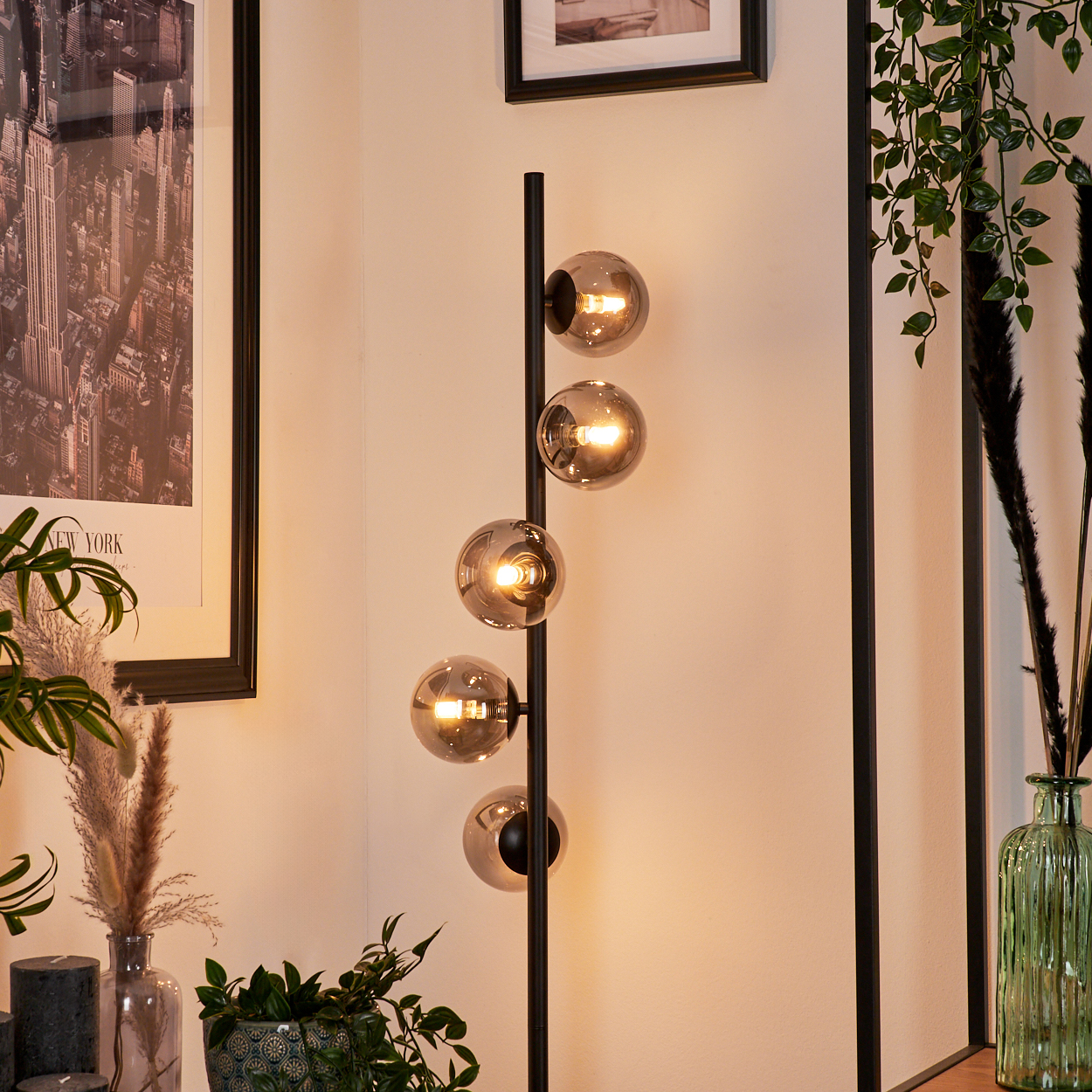 Eine moderne Stehlampe mit fünf Glaskugelschirmen. An der Wand hängt ein New York-Poster, und im Vordergrund befinden sich Pflanzen.