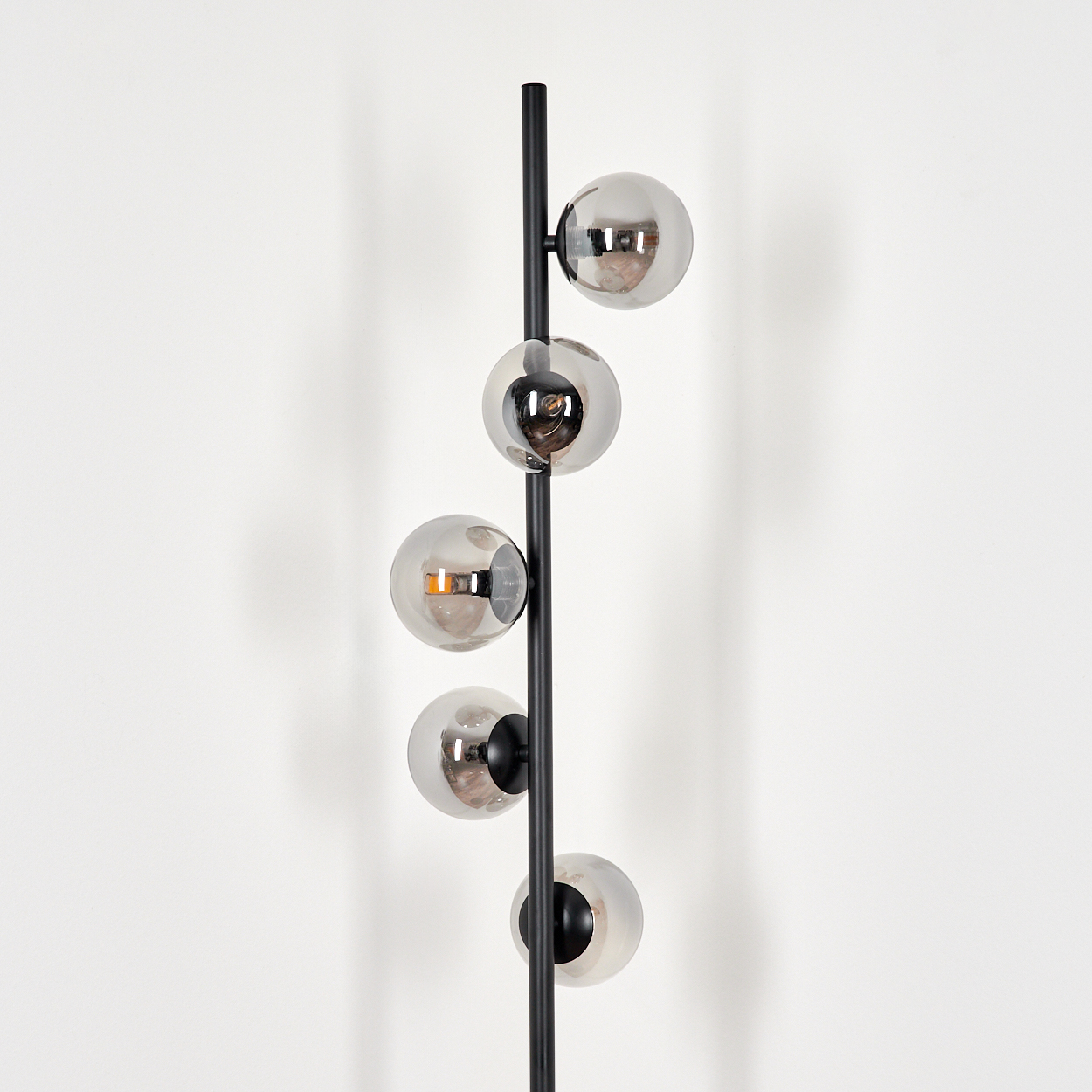 Eine schwarze Stehlampe mit fünf kugelförmigen, verspiegelten Glasschirmen. Die Lampe steht vor einer weißen Wand, das Licht reflektiert sich.