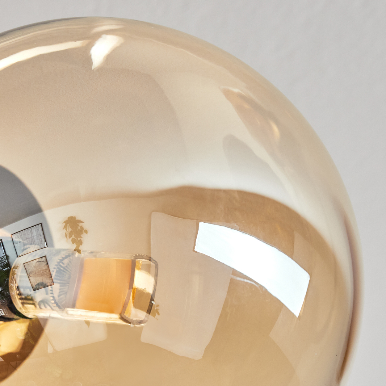 Nahaufnahme einer reflektierenden, bernsteinfarbenen Glaskugel. Innen spiegeln sich Kunst, Pflanzen und ein helles Rechteck.
