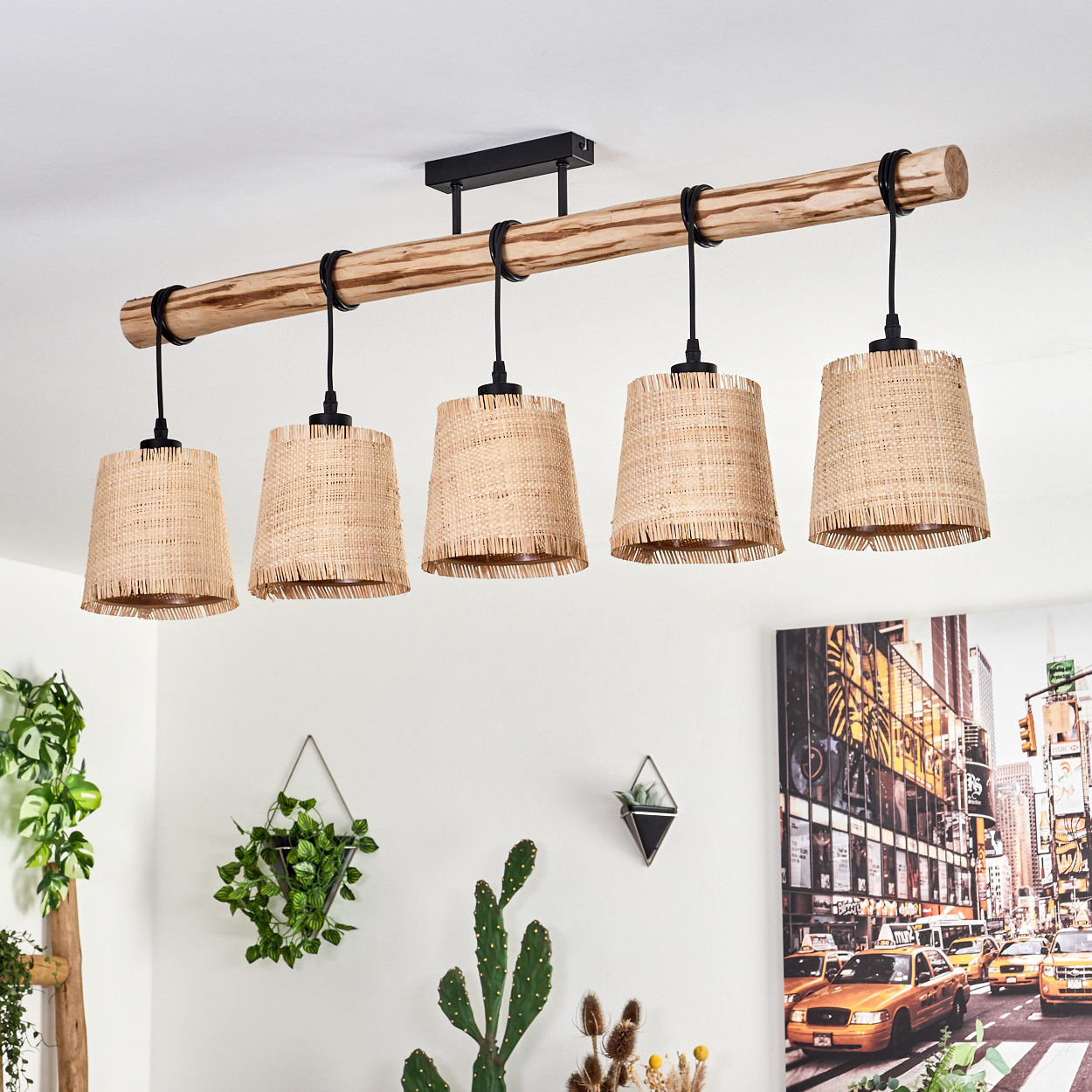 Ein Holzbalken mit fünf gewebten Lampen hängt von der Decke. Pflanzen und ein Gemälde mit Stadtszene sind im Hintergrund zu sehen.