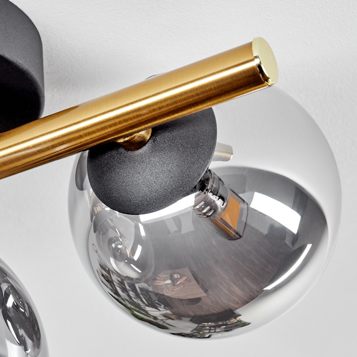 Nahaufnahme einer modernen Lampe. Sie hat einen goldenen Balken, einen schwarzen Sockel und eine transparente Glaskugel.