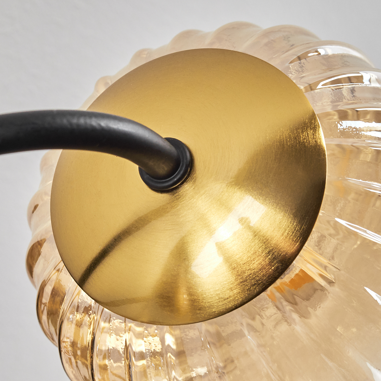 Nahaufnahme einer goldfarbenen Lampenhalterung mit schwarzem Arm. Die Lampe hat einen gerippten Glasschirm.