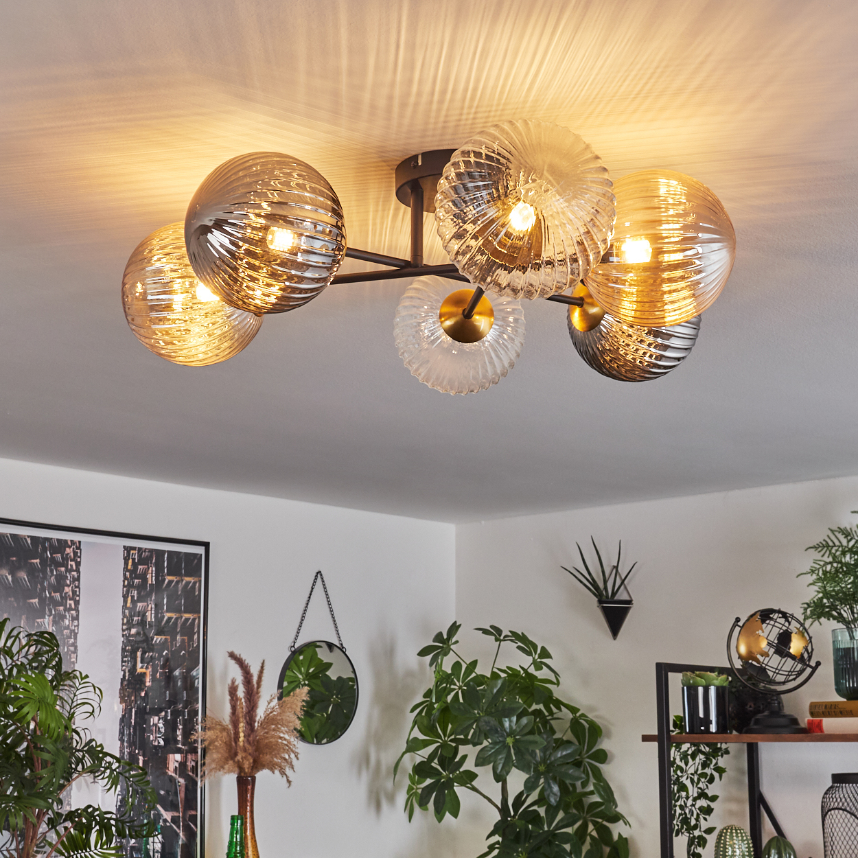 Eine moderne Deckenlampe mit Glaskugeln. Dekorative Pflanzen und ein Spiegel befinden sich im Raum. Die Lampe ist eingeschaltet und beleuchtet den Raum.