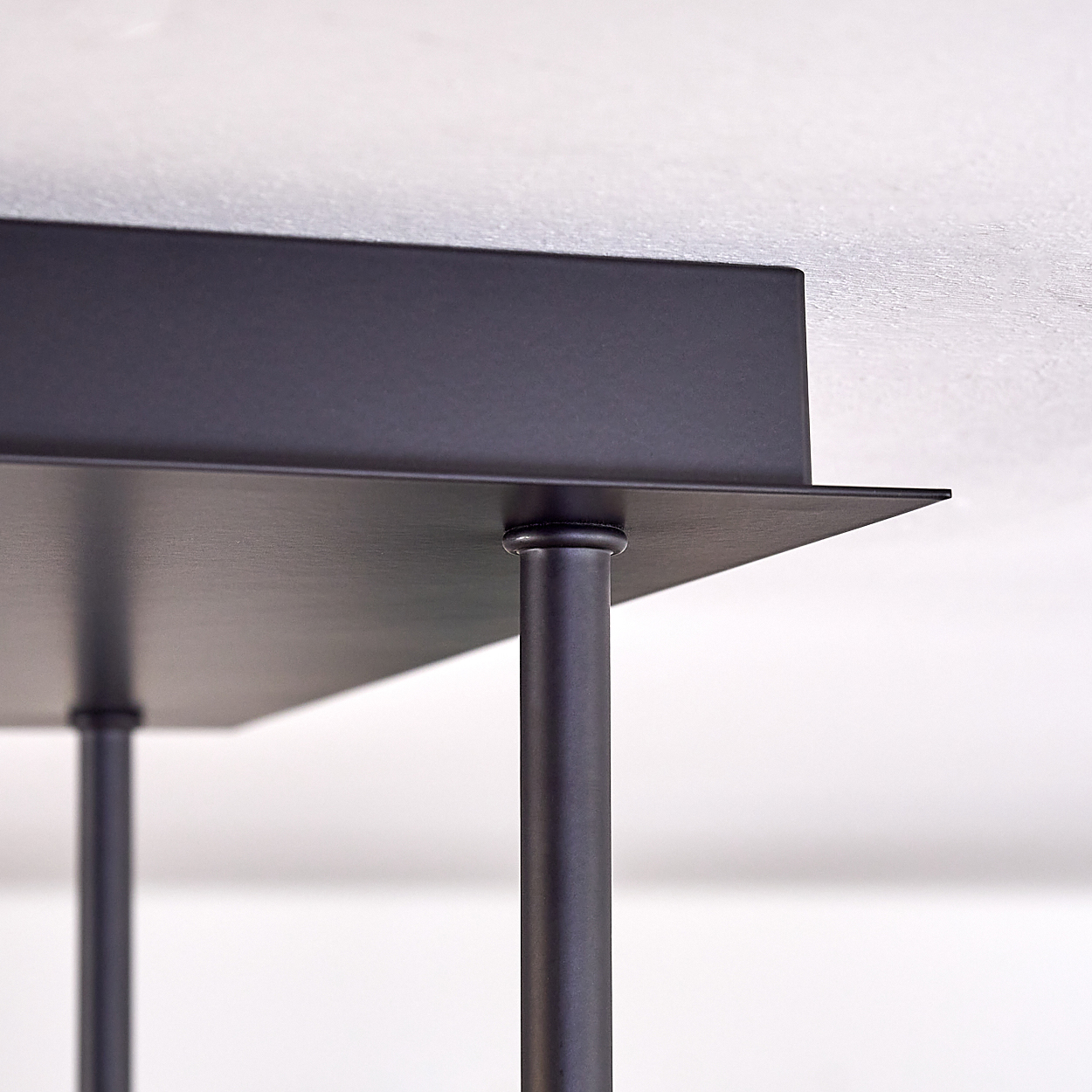 Nahaufnahme einer schwarzen Metallkonstruktion. Sie hat eine rechteckige Oberseite, die von zylindrischen Beinen getragen wird. Der Hintergrund ist eine weiße Decke.