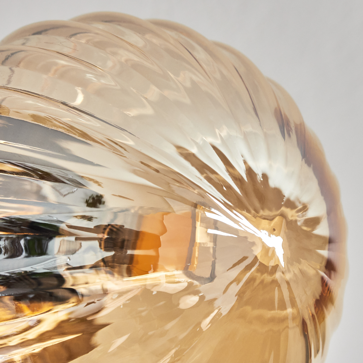 Nahaufnahme einer Leuchte. Sie hat eine klare, gerippte, glasartige Oberfläche mit goldbraunem Farbton. Der Hintergrund ist weiß.