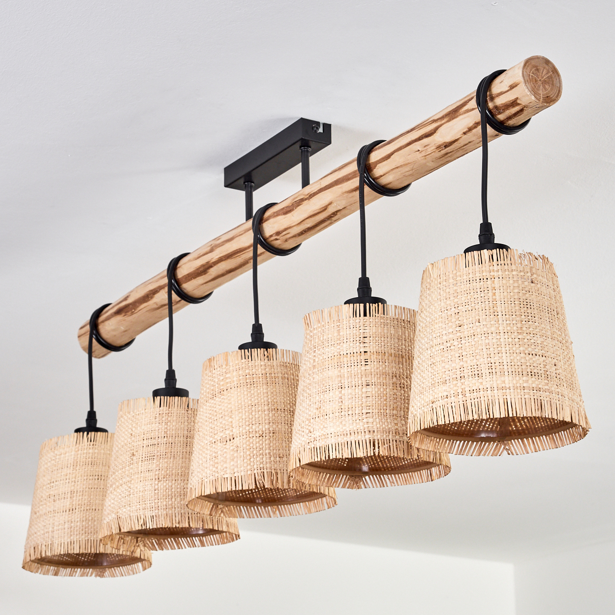 Ein Holzbalken mit fünf Pendelleuchten. Jede Leuchte hat einen gewebten Schirm. Die Leuchten hängen mit schwarzen Drähten vom Balken.