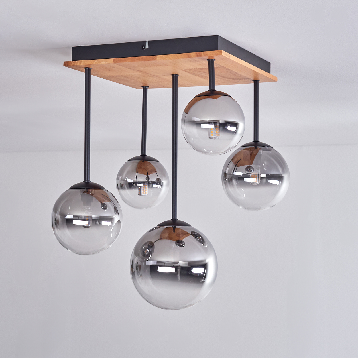 Eine moderne Deckenleuchte mit vier Glaskugeln. Die Leuchte hat eine Holzbasis und schwarze Metallstangen, die Kugeln sind reflektierend.