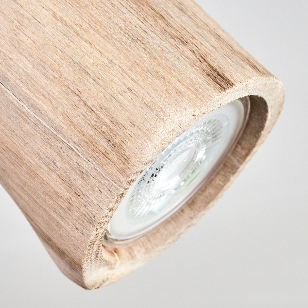 Nahaufnahme einer Holzlampe. Die Lampe hat einen zylindrischen Holzkörper und ein helles LED-Licht. Der Hintergrund ist schlicht weiß.