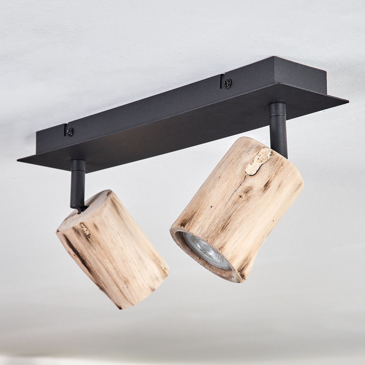 Eine Deckenleuchte mit zwei Holzspots. Sie hat einen schwarzen Metallrahmen und ist an einer weißen Decke montiert.