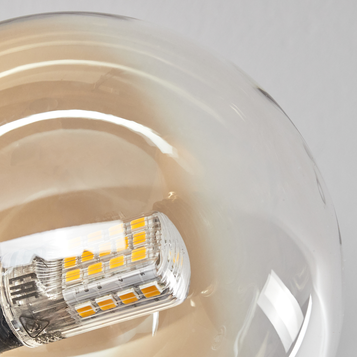 Nahaufnahme einer Glühbirne mit LED-Array. Die Birne ist transparent mit warmem Bernsteinton. Der Hintergrund ist hellgrau.