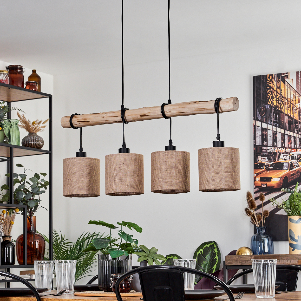 Ein Holzbalken mit 4 Lampenschirmen hängt über einem Tisch mit Gläsern und Pflanzen. Ein Gemälde und Regale mit Gläsern sind im Hintergrund.