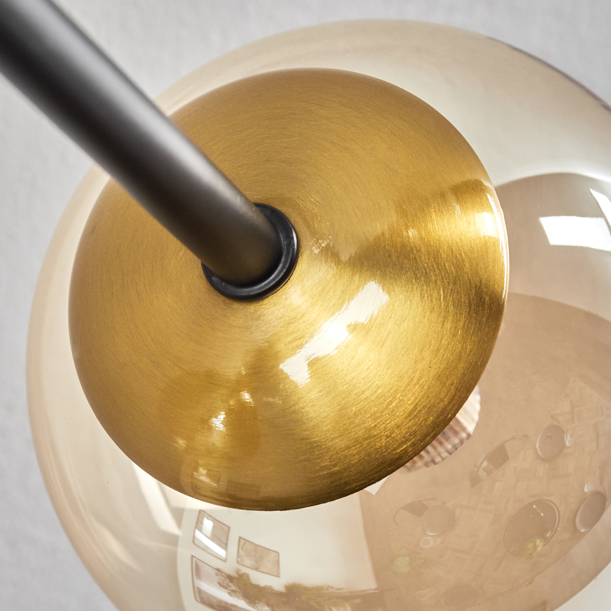 Nahaufnahme einer Leuchte. Eine goldene Scheibe ist mit einer schwarzen Stange verbunden, mit einer transparenten, bernsteinfarbenen Glaskugel.