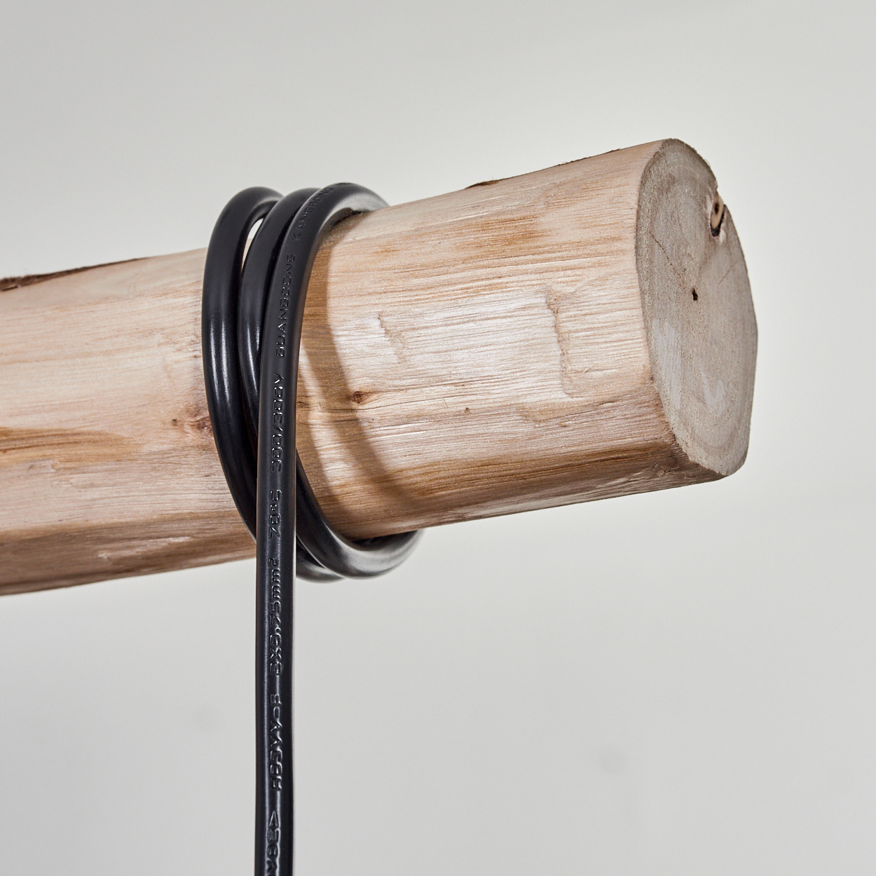 Ein schwarzes Kabel ist um einen Holzstamm gewickelt. Der Stamm hat eine hellbraune Farbe und befindet sich auf einem schlichten weißen Hintergrund.