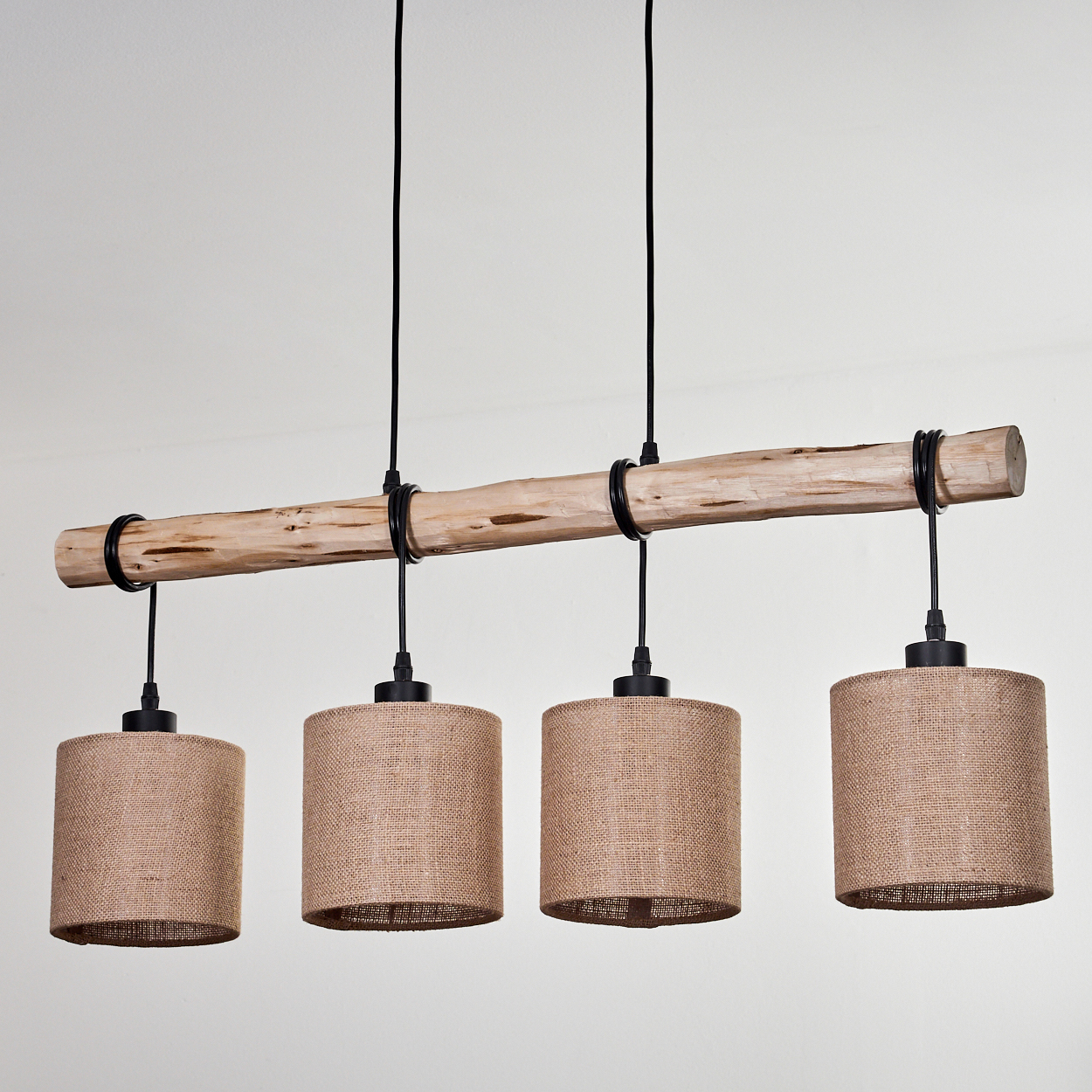 Ein Holzbalken mit vier darunter hängenden Jutegarnlampen. Der Balken wird von schwarzen Ringen getragen. Der Hintergrund ist eine schlichte weiße Wand.