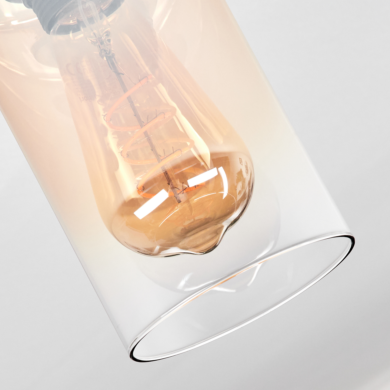 Nahaufnahme einer Glühbirne in einem Glaszylinder. Die Birne ist orange, das Glas ist klar. Der Hintergrund ist weiß.