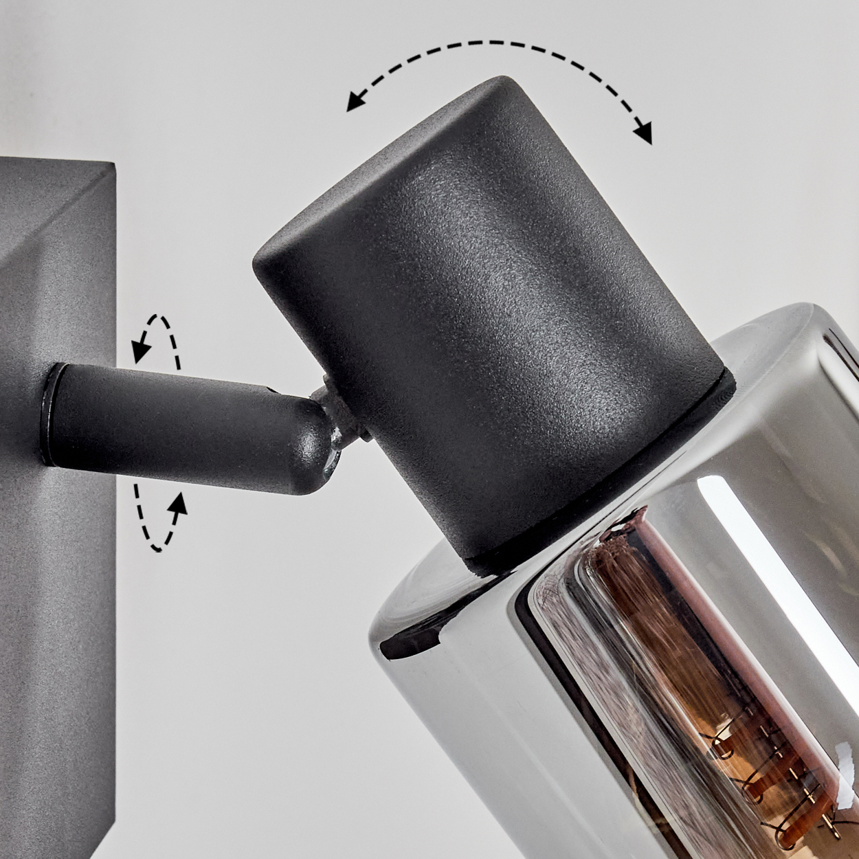 Ein verstellbarer schwarzer und verchromter Strahler ist an einer Wand montiert. Pfeile zeigen die Drehfähigkeit der Lampe an.