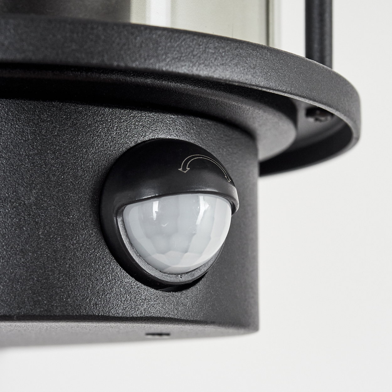 Nahaufnahme einer schwarzen Außenlampe mit Bewegungssensor. Der Sensor ist eine graue Kuppel mit Pfeil. Der Hintergrund ist weiß.