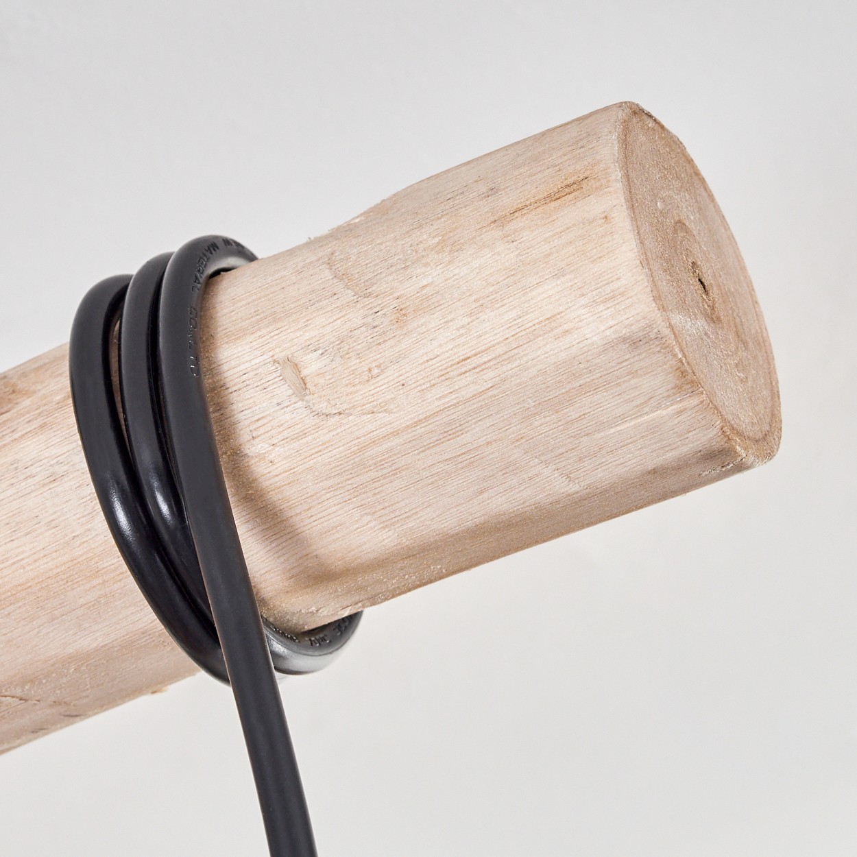 Ein Holzbalken ist mit einem schwarzen Kabel umwickelt. Der Balken ist hellbraun, und das Kabel ist um den Balken gewickelt.