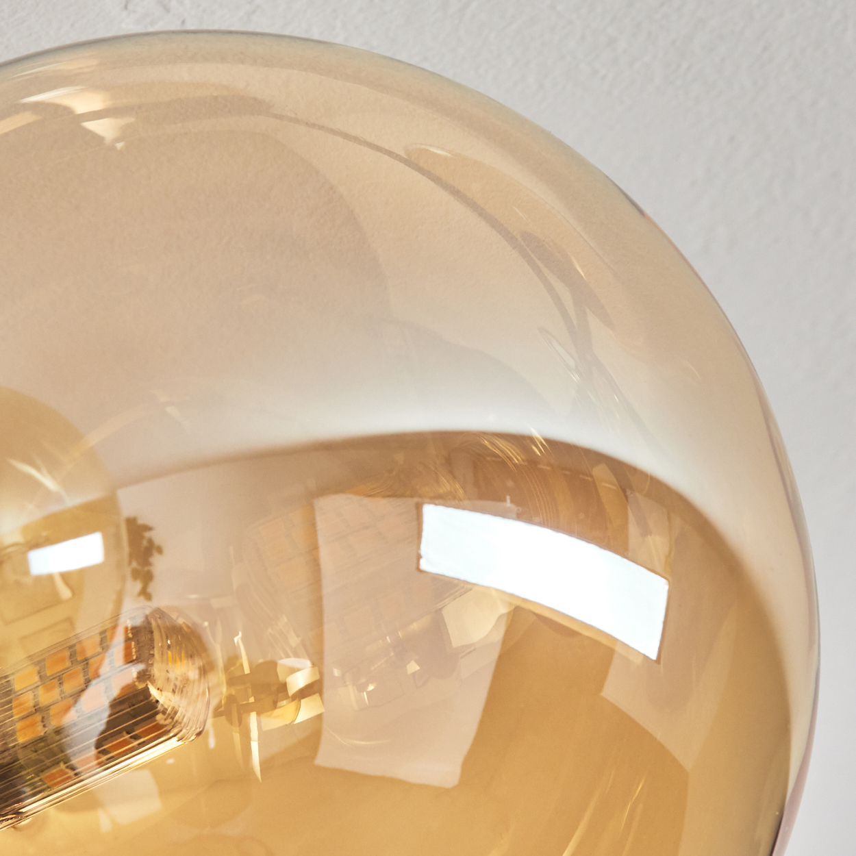 Nahaufnahme einer Glühbirne. Die Birne hat eine transparente bernsteinfarbene Farbe und reflektiert Licht und Umgebung auf weißem Hintergrund.
