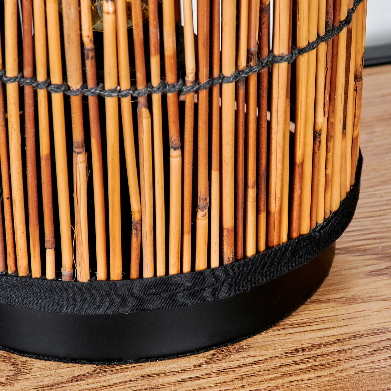Nahaufnahme einer Bambuslampe. Braune Bambusstäbe bilden den Schirm, schwarzer Sockel, auf Holzoberfläche.