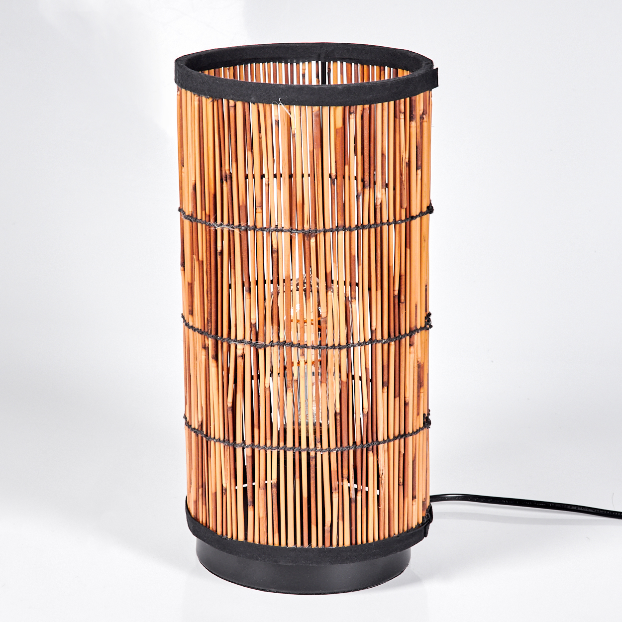 Eine zylindrische Lampe aus Bambusstäben. Die Lampe hat einen schwarzen Sockel und einen schwarzen oberen Rand. Die Glühbirne ist innen sichtbar.