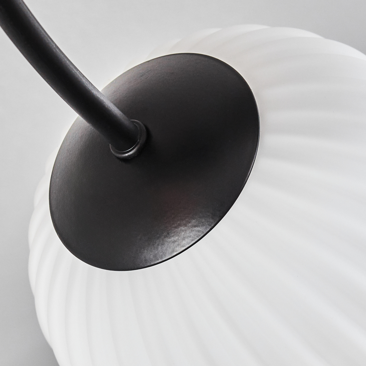 Nahaufnahme einer Lampe mit schwarzem Metallarm und weißem, geripptem Glaskolben vor hellgrauem Hintergrund.