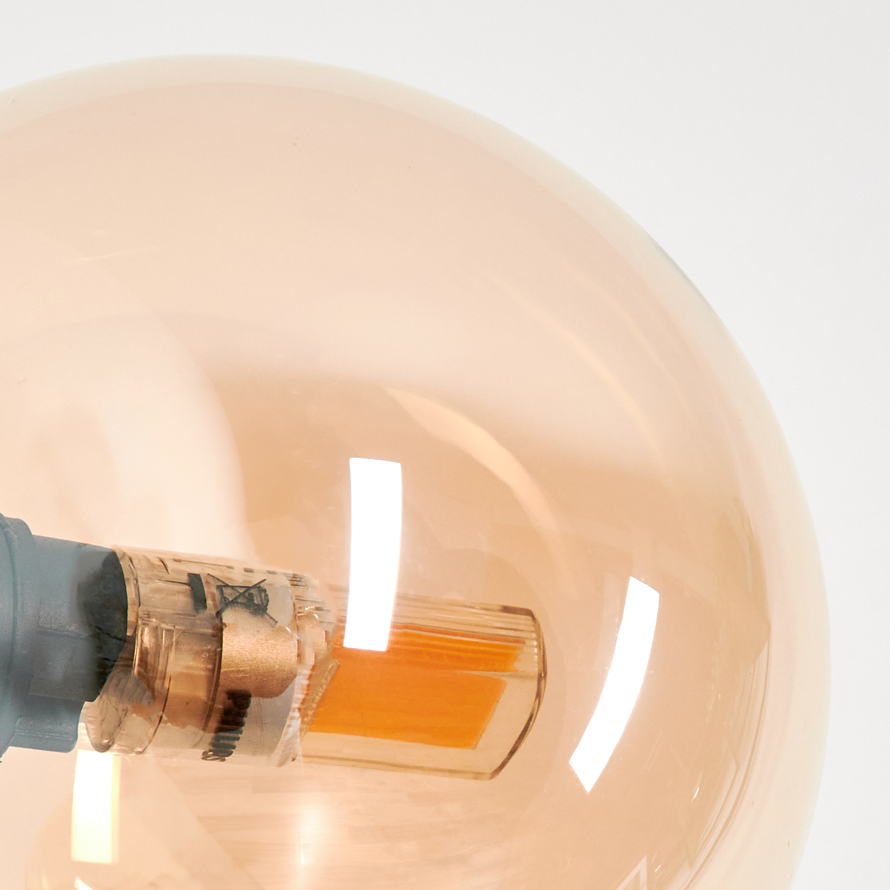 Nahaufnahme einer Glühbirne. Die Birne ist transparent und orange, mit einem inneren orangefarbenen Leuchtelement und einem grauen Sockel.