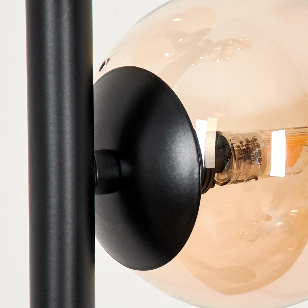 Nahaufnahme einer modernen Lampe. Eine schwarze Stange trägt eine große, bernsteinfarbene Glühbirne. Eine schwarze Metallscheibe hält die Birne.