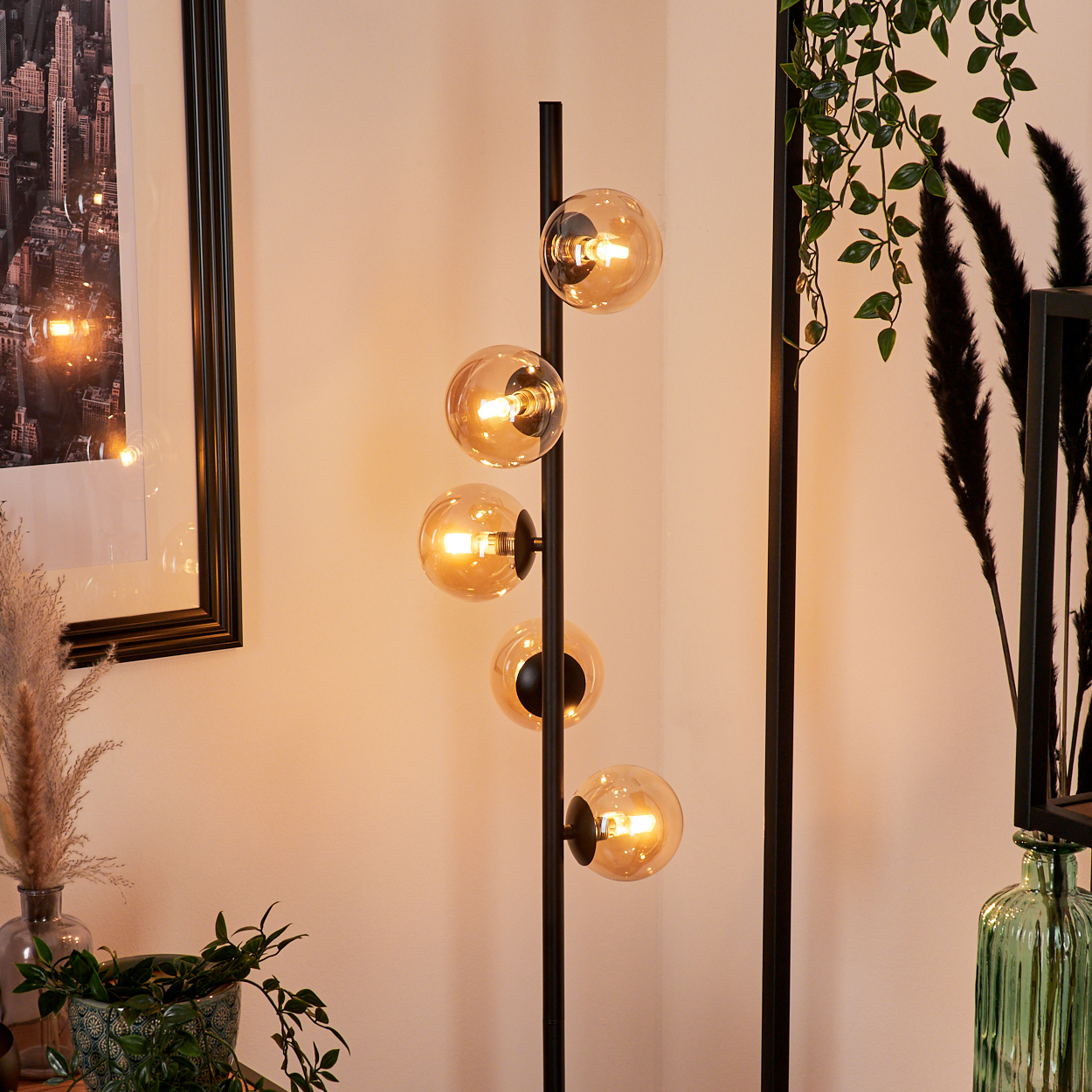 Eine Stehlampe mit fünf leuchtenden Kugeln ist der Mittelpunkt. Drumherum sind dekorative Pflanzen, gerahmte Kunst und Vasen.