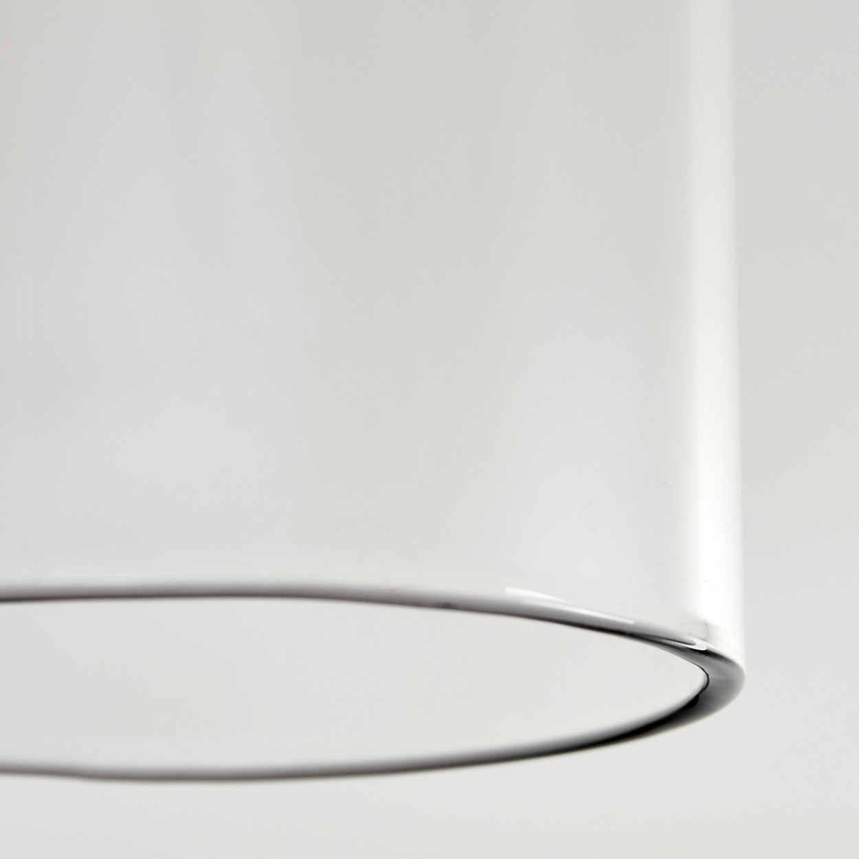 Nahaufnahme eines transparenten Glaszylinders mit schwarzem Rand vor weißem Hintergrund. Das Glas reflektiert Licht.