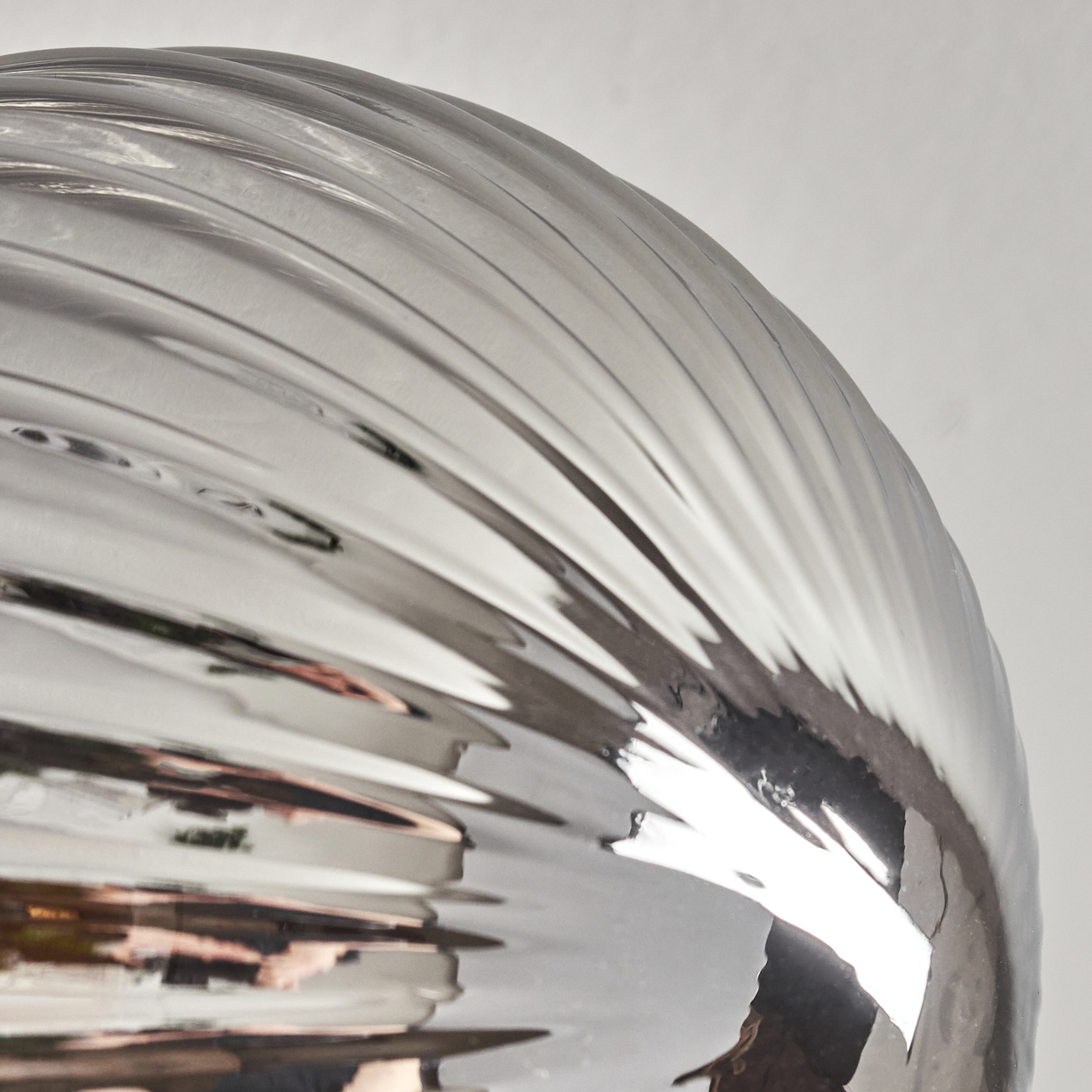 Nahaufnahme eines glänzenden, silbernen Objekts mit geriffelter Oberfläche, das Licht vor einem neutralen Hintergrund reflektiert.