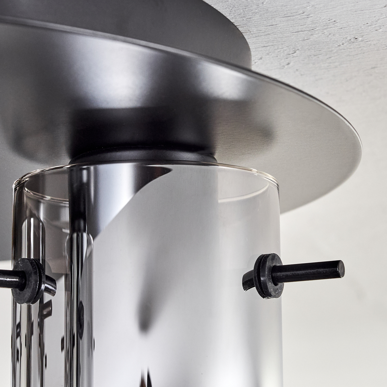 Nahaufnahme einer modernen Lampe. Sie hat einen Chromzylinder, schwarze Kreiselemente und eine flache schwarze Scheibe. Der Hintergrund ist weiß.
